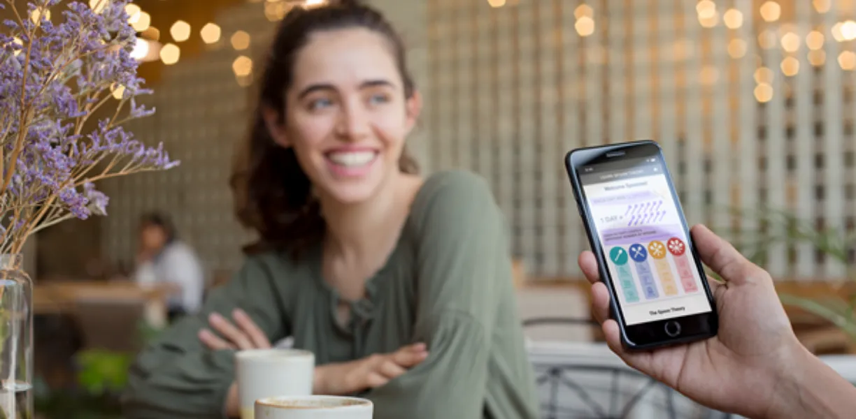 Man holding phone with Spoonie Day app at a table with a woman.